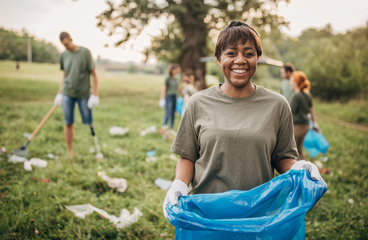 A woman holding a blue bag in the grass.